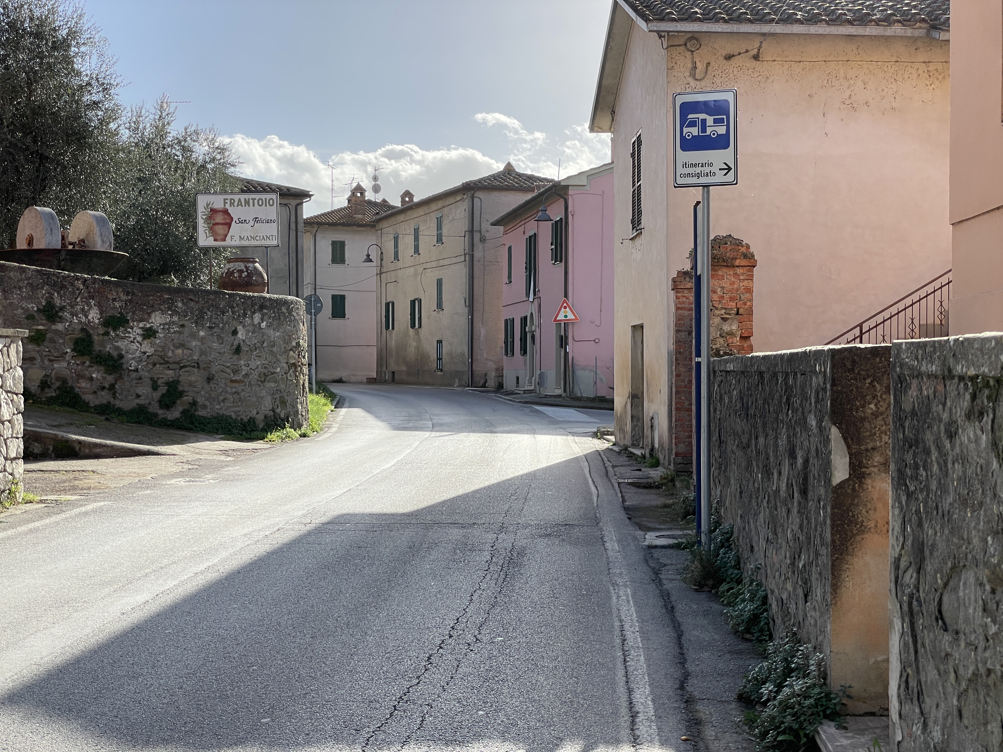 Entrance to San Feliciano on a paved road between pastel houses. A sign gives the indication of “recommended route” for campers.